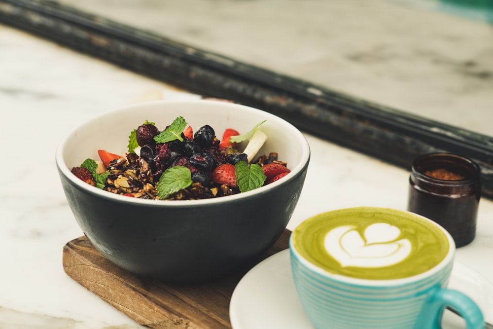 Ensalada de bayas en cuenco de cerámica negra junto a café capuchino