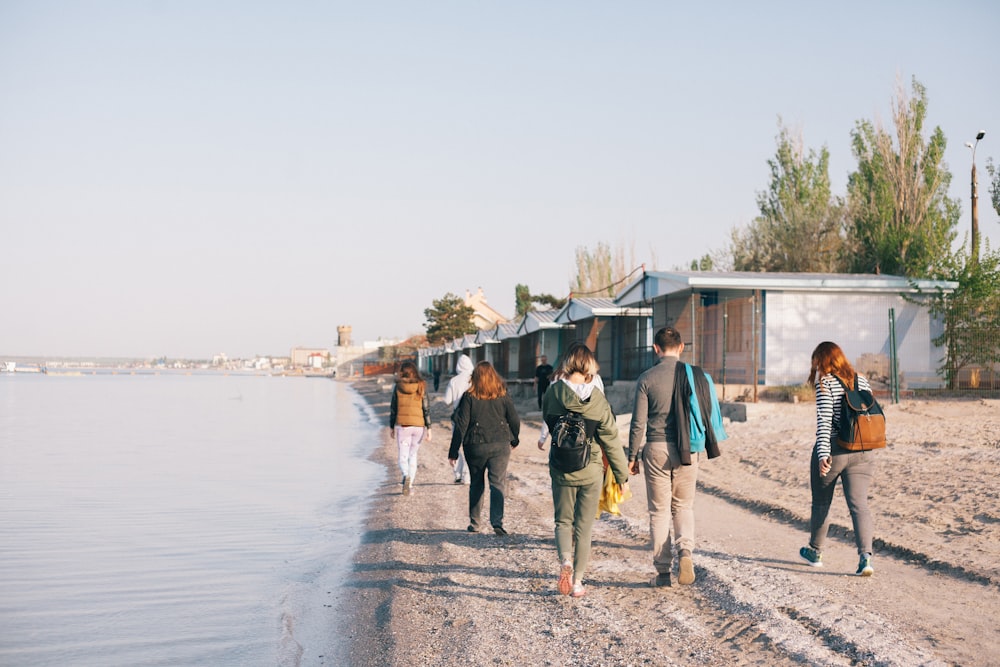 people walking beside seashore towards houses at daytime