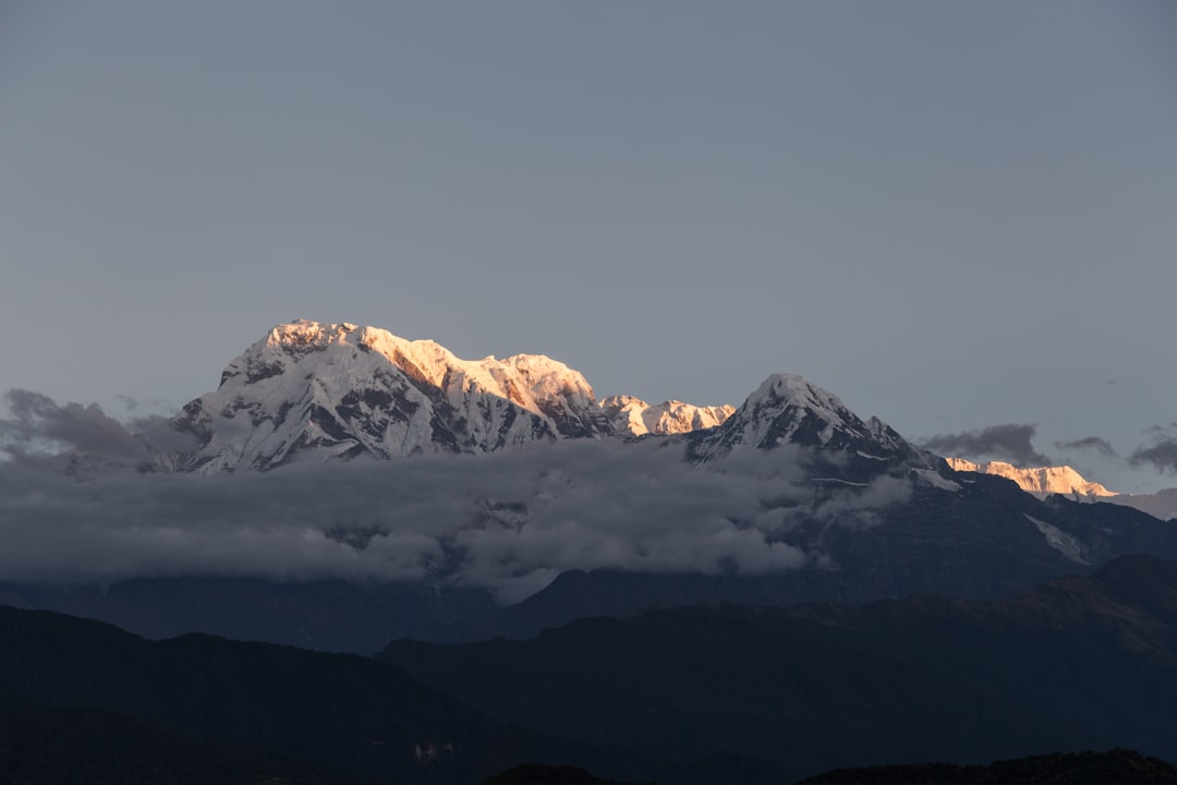snow mountain under cloudy sky, We had to wake up quite early. Hiking partly in the cover of the night, using the flashlights to light the path to reach the top of the hill. We were there right on time to see the sun slowly bathing the peaks of Annapurna.<p></figure>It was really magnificent view as the sun slowly reaches the peaks and gray turns into orange and finally white.</p><p>The mountains that inspired so many artists, battled with so many alpinists and provided shelter to so many people in need.
