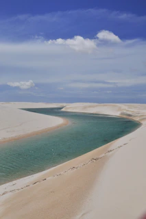 A stunning turquoise lagoon surrounded by white sand dunes under a bright blue sky.