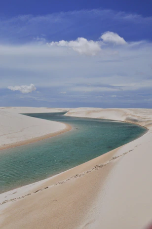A stunning turquoise lagoon surrounded by white sand dunes under a bright blue sky.