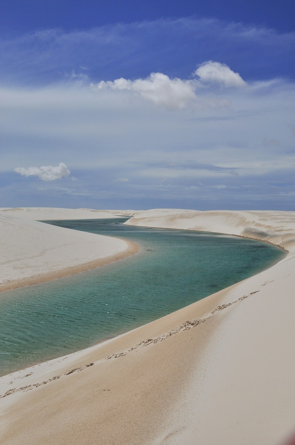 body of water between sand under cloudy sky