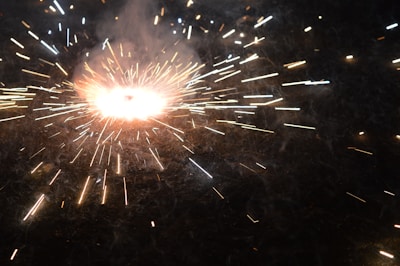 Bright, radiating sparks and light burst outward from a central point against a dark background, creating a dynamic and energetic pattern reminiscent of a fireworks display or an intense explosion.