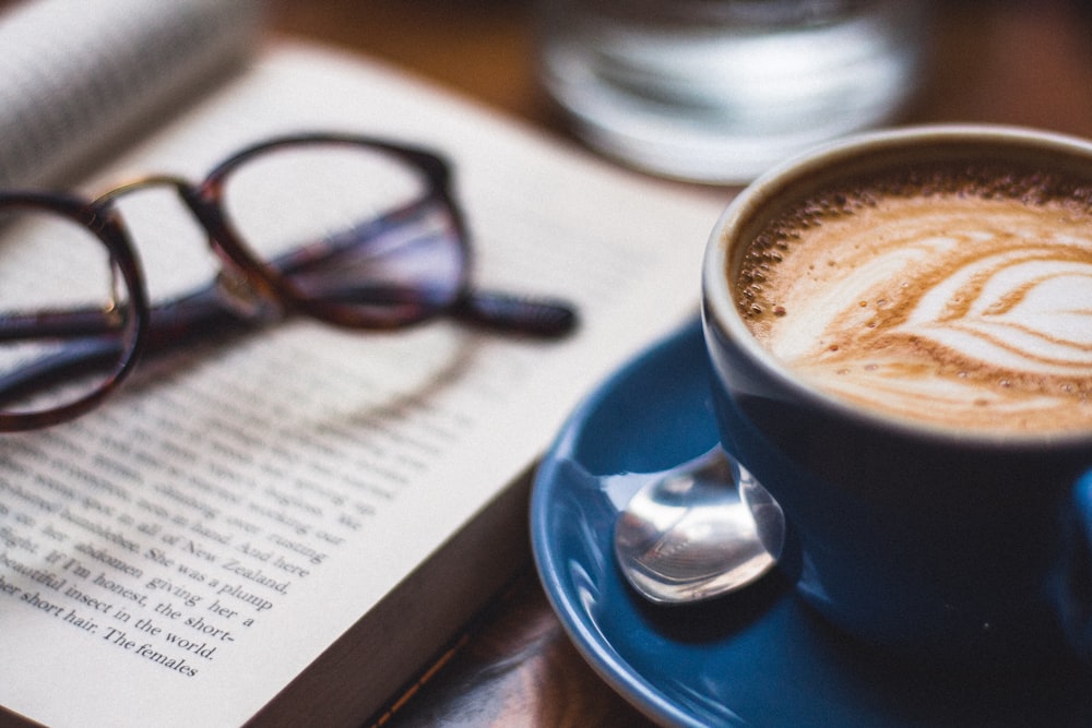 black framed eyeglasses on book beside cappuccino