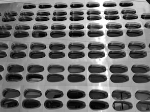 A modern architectural facade with a grid of oval-shaped reflective windows arranged in a repetitive pattern. The surface appears metallic and slightly glossy, with a sleek, futuristic design.