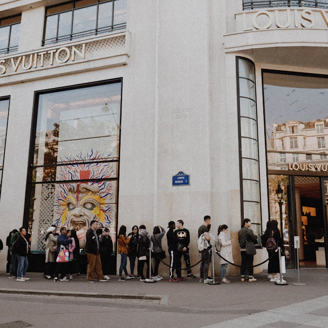 People standing in a queue along the outside of a Louis Vuitton store