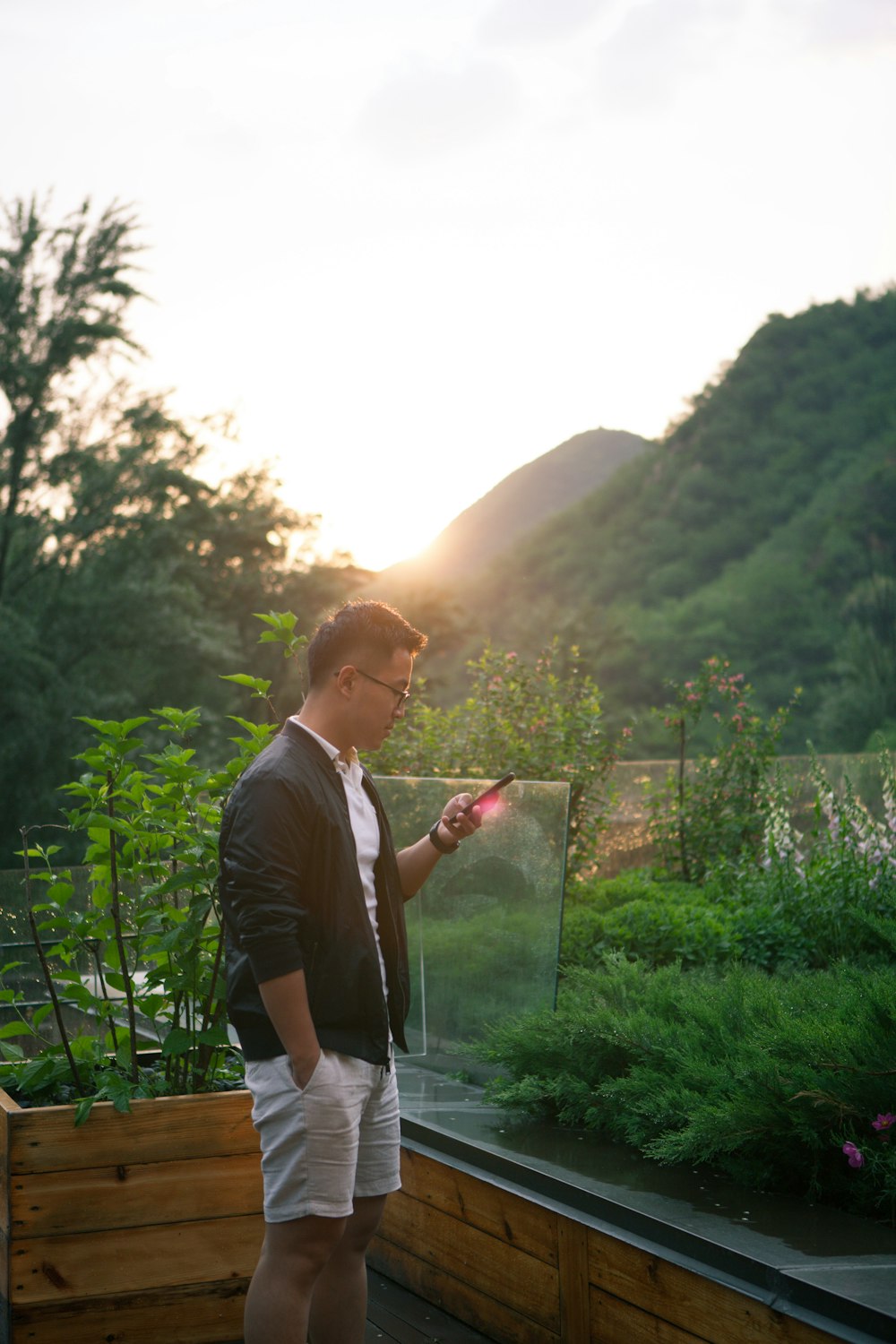 man standing beside glass wall while using smartphon e