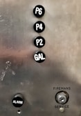 A metallic panel with elevator buttons labeled P6, P4, P2, and GAL in a vertical alignment. Below the buttons, there is a black button labeled ALARM and a keyhole labeled as FIREMANS SERVICE.