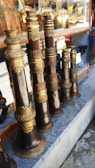 Several intricately designed musical instruments with ornate golden and bronze detailing are arranged on a stone shelf. Behind the instruments, there are reflections and glimpses of other metallic items, possibly more instruments or decorative objects.