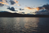 A serene lake reflecting the surrounding mountains during sunset.