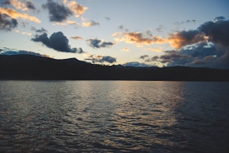 A wide-angle shot of a calm lake at sunset, reflecting colorful skies and distant mountains.