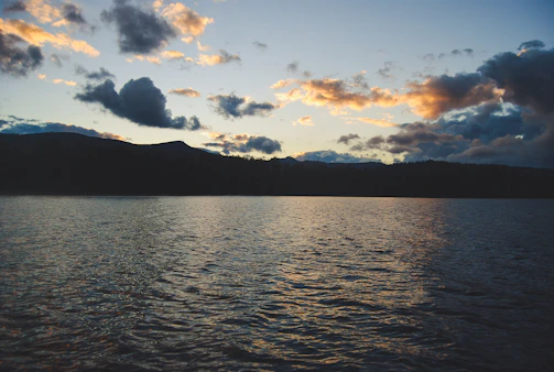 A serene lake reflecting the colorful hues of a sunset with mountains in the background.
