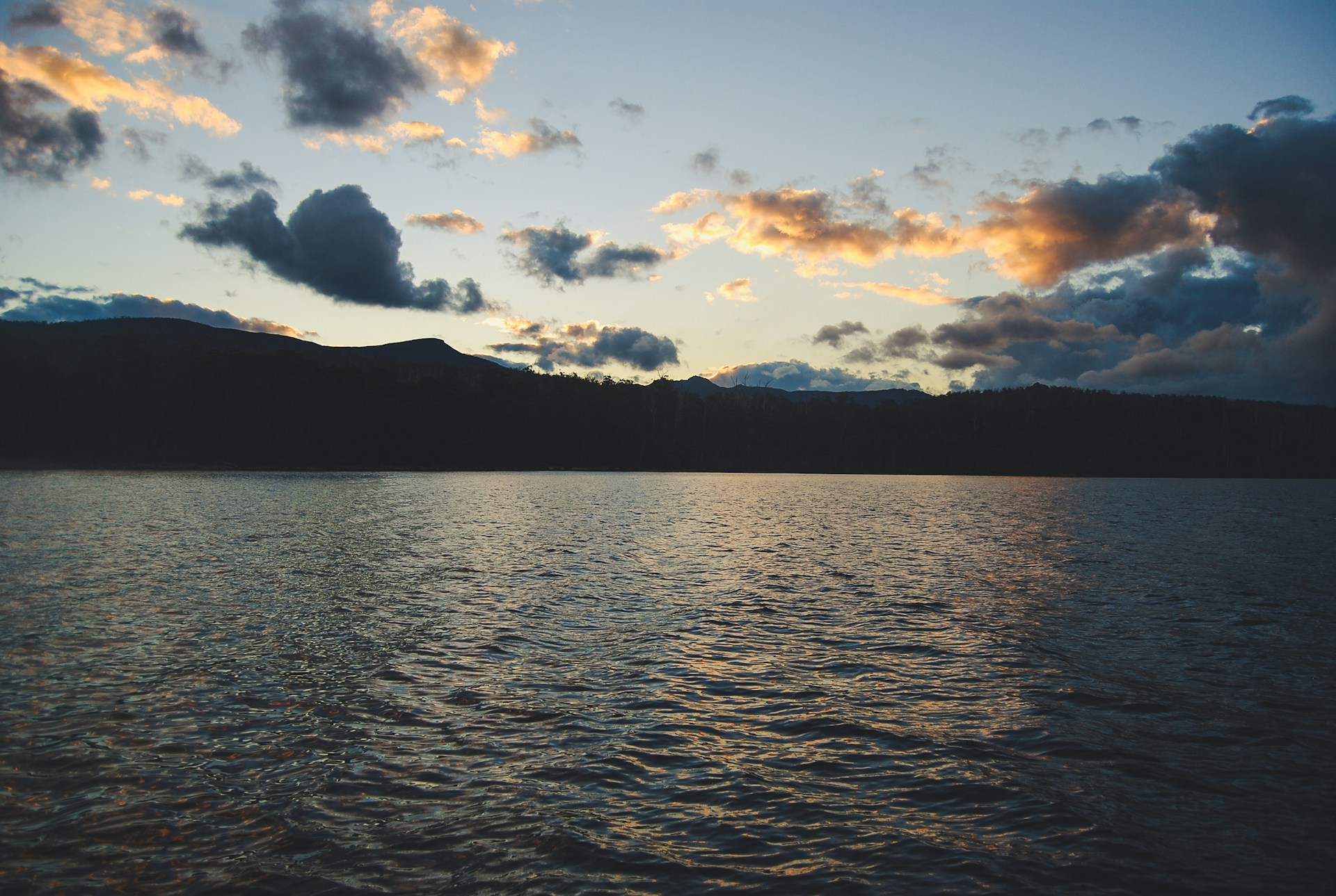 A serene mountain lake reflecting deep purple and golden yellow hues of the sky, inviting peaceful exploration.