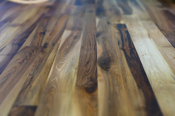 Warm-toned hardwood flooring in a cozy living room with sunlight streaming through large windows.