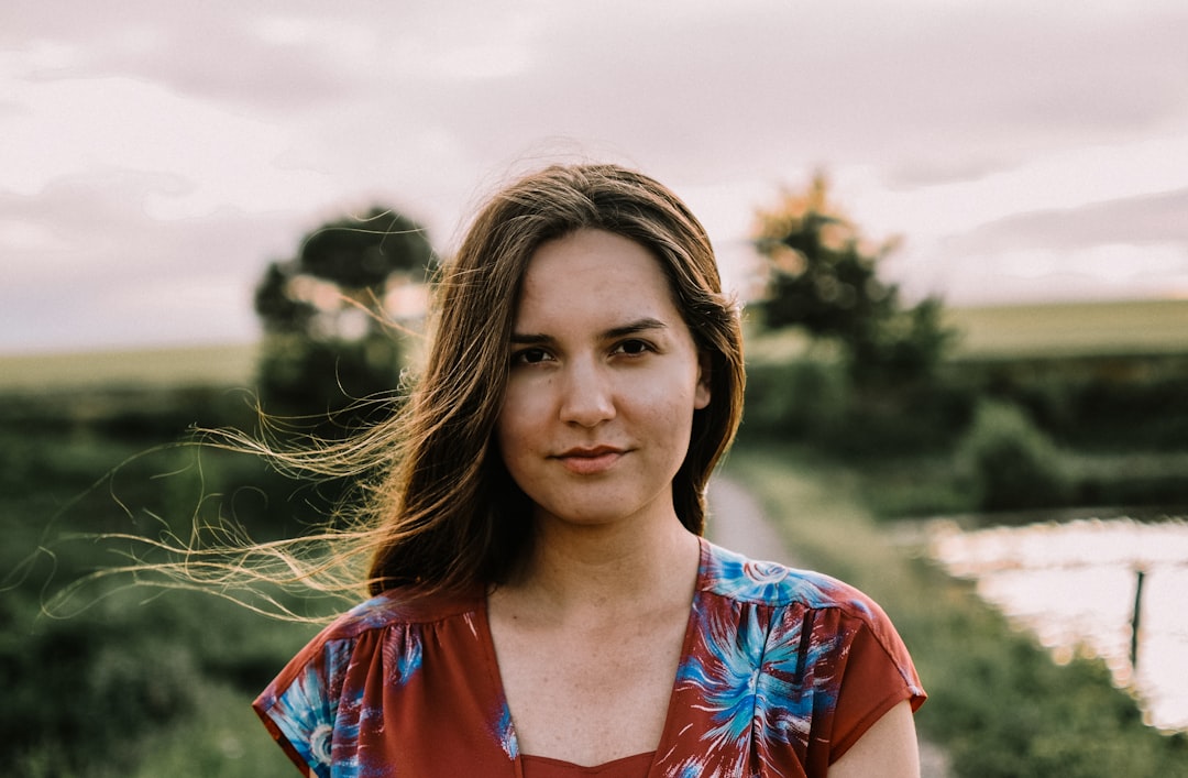 selective focus photography of woman wearing square-neck top standing near body of water and pthway