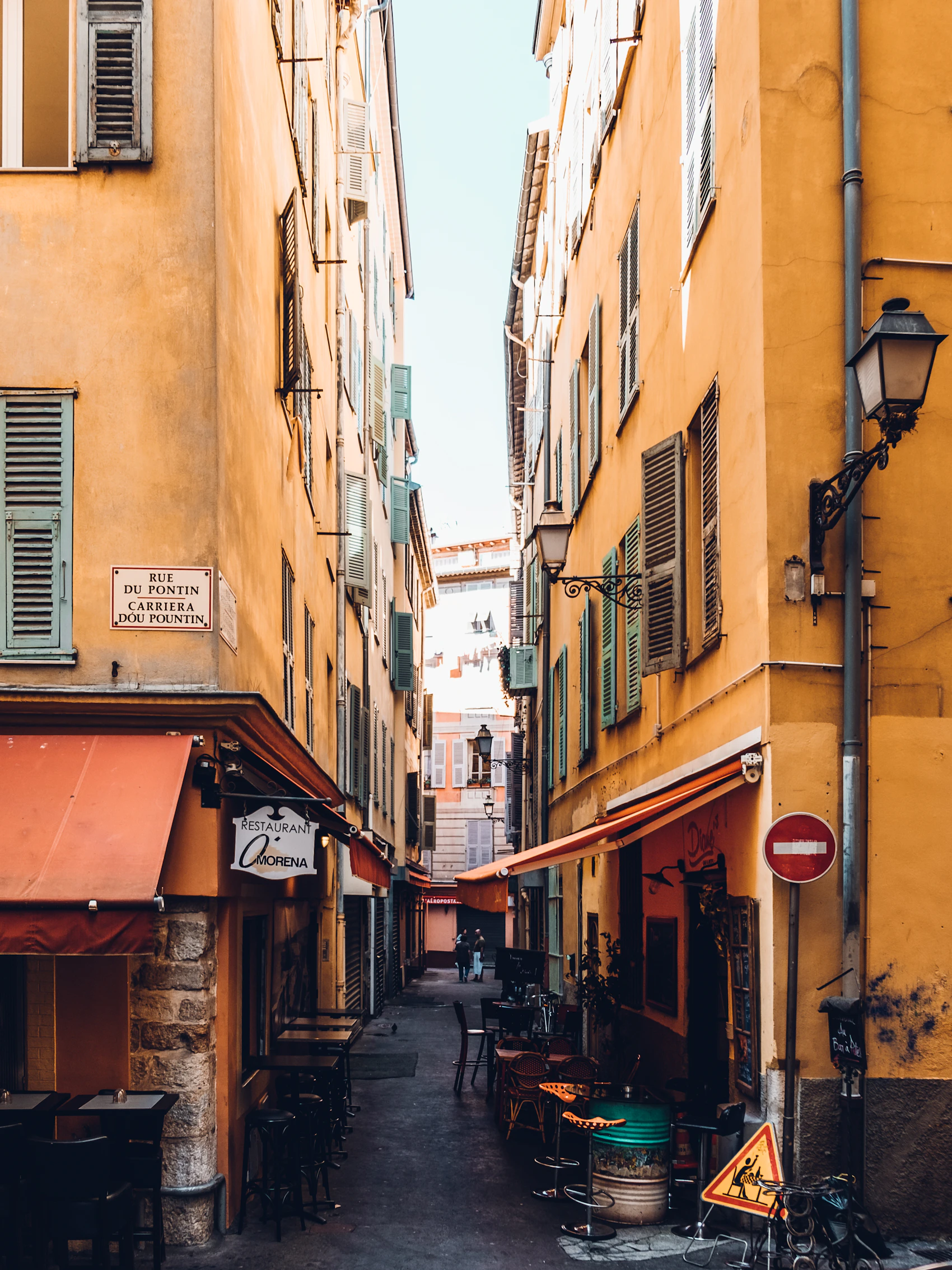 A quiet restaurant lane between ochre buildings in Vieux Nice