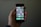 A hand is holding a smartphone displaying a home screen with various app icons. The apps include settings, phone, messages, and several others arranged in a grid pattern. The background is dimly lit, highlighting the phone and hand.