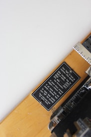 A close-up view of a wooden plaque with a metal label attached using screws. The label contains technical instructions related to heating and temperatures, mentioning terms like 250°F, 270°F, and 239°F. The metal part adjacent to the label shows part of a measuring or display device, possibly a thermometer or gauge.