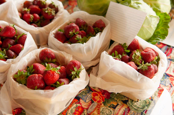 A close-up of a fresh strawberry basket with a handwritten note and a phone beside it.