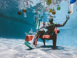 man sitting on chair underwater with floating bottles
