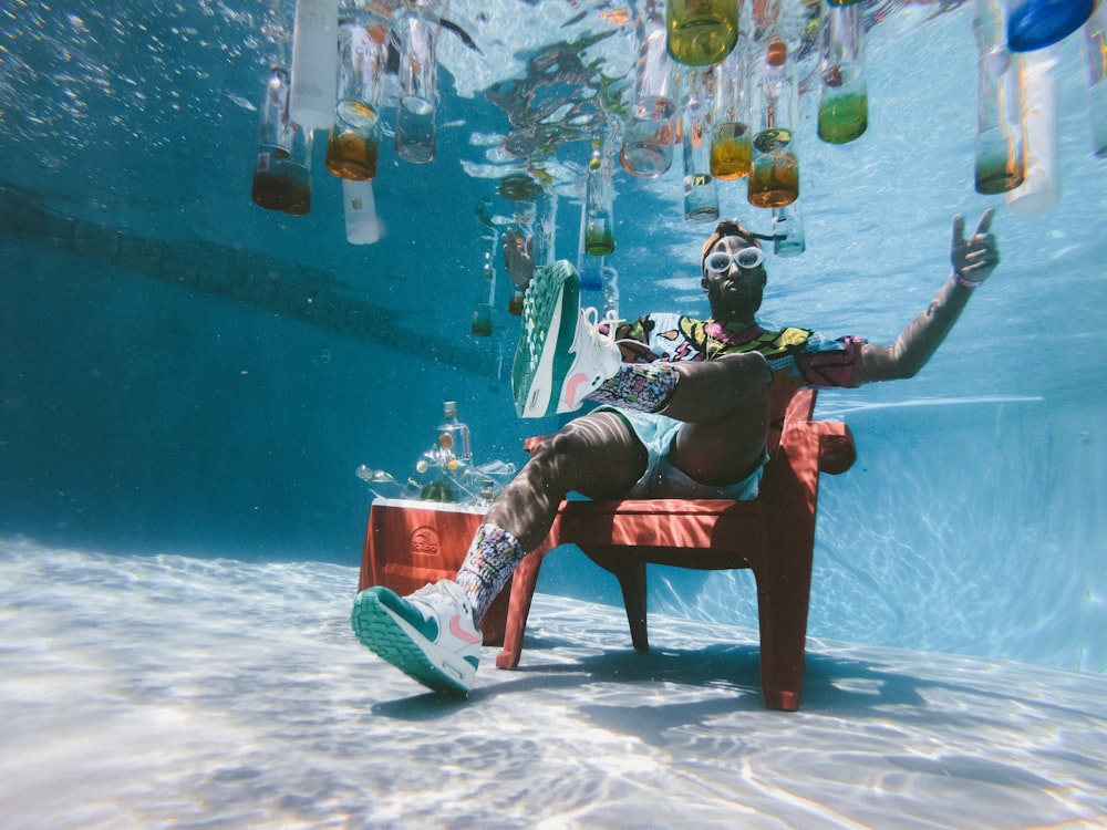 Mann sitzt auf Stuhl unter Wasser mit schwimmenden Flaschen