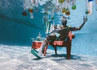 man sitting on chair underwater with floating bottles