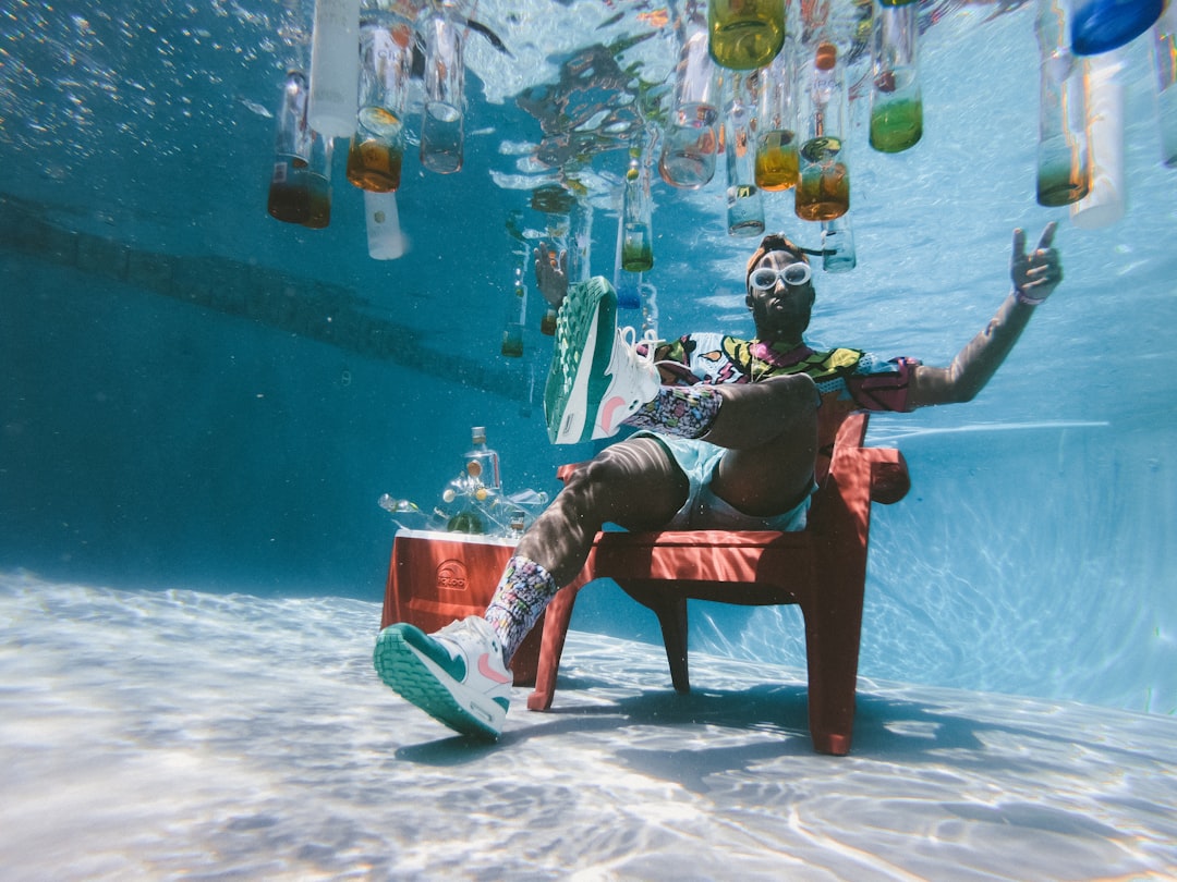 man sitting on chair underwater with floating bottles, Pool Full Of Liquor
