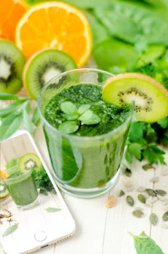 A refreshing green avocado smoothie in a clear cup with condensation, surrounded by fresh avocado halves and leaves.