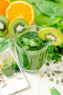 Healthy green smoothie and fresh fruits on a white kitchen counter