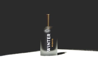 A perfume bottle with a sleek, dark-to-light gradient design and text reading 'Winter Nights'. The bottle features a golden cap and is set against a dark background with light highlighting its form.