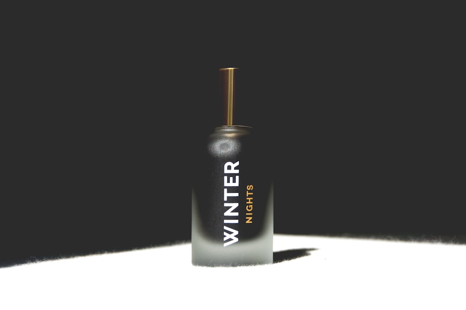 A perfume bottle with a sleek, dark-to-light gradient design and text reading 'Winter Nights'. The bottle features a golden cap and is set against a dark background with light highlighting its form.