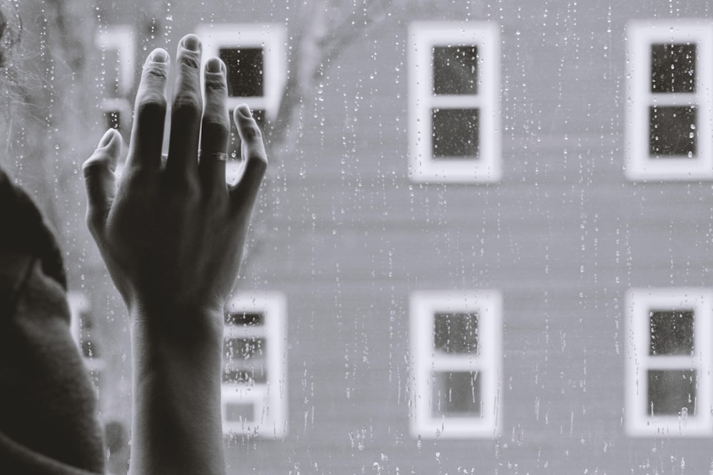 grayscale photo of person holding glass window while raining