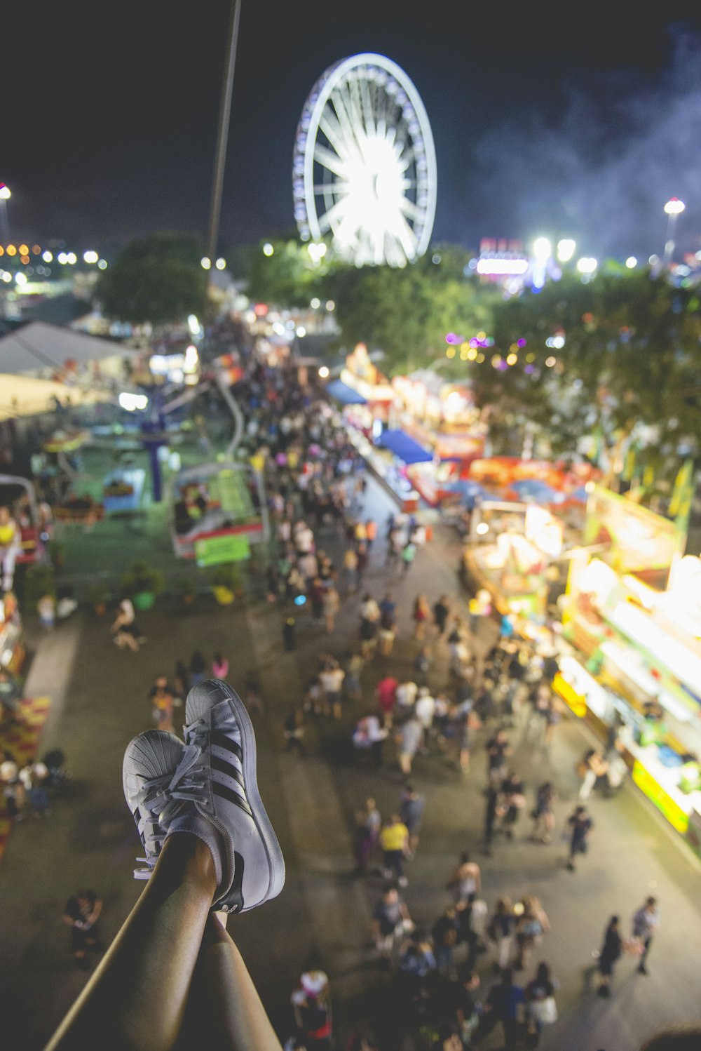 selective focus photo of person wearing sneakers and ferris wheel at distance