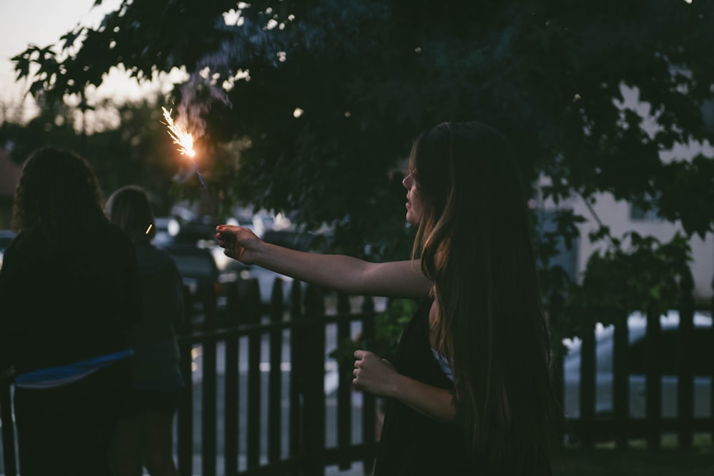 woman holding sparkler near fence
