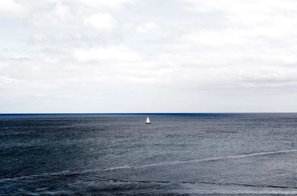 white sailboat on ocean under cloudy sky during daytime