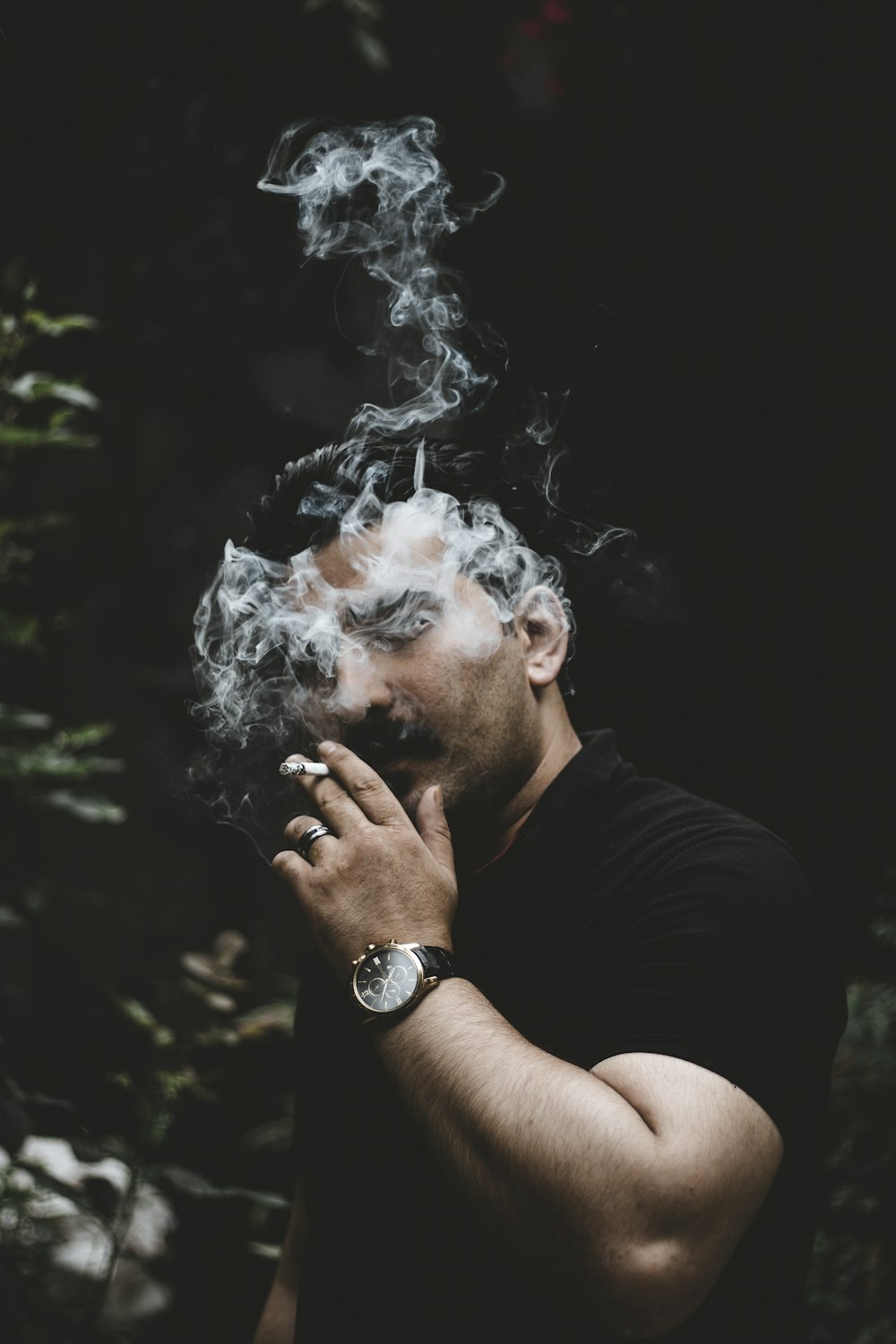 man smoking beside green leafed plants