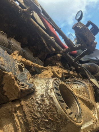 Close-up of a muddy off-road vehicle, showcasing its intricate mechanical parts covered in dirt. The angle gives a dynamic and rugged appearance, highlighting the resilience and adventure associated with off-road driving.