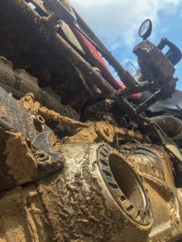 Close-up of a muddy off-road vehicle, showcasing its intricate mechanical parts covered in dirt. The angle gives a dynamic and rugged appearance, highlighting the resilience and adventure associated with off-road driving.