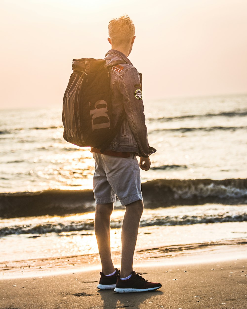 man carrying backpack standing near shoreline