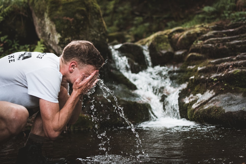man wash his face at the body of water during daytime