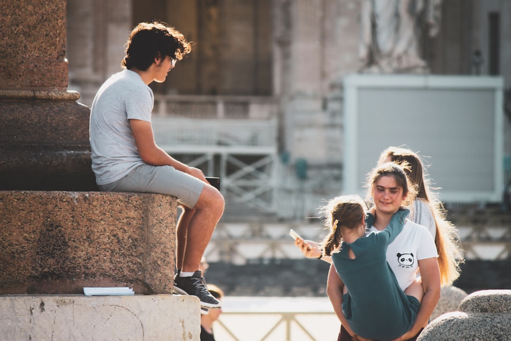 man sitting beside pillar facing two women and girl