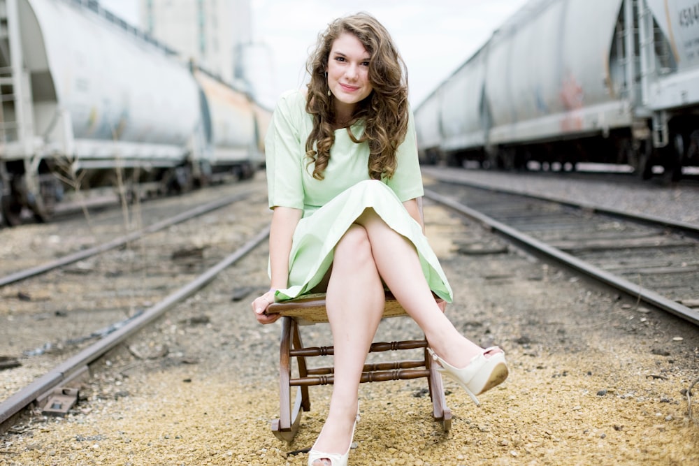 girl sitting on chair between train tracks during day