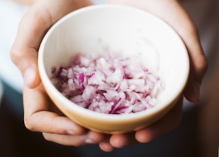 person holding ceramic bowl filled with onions