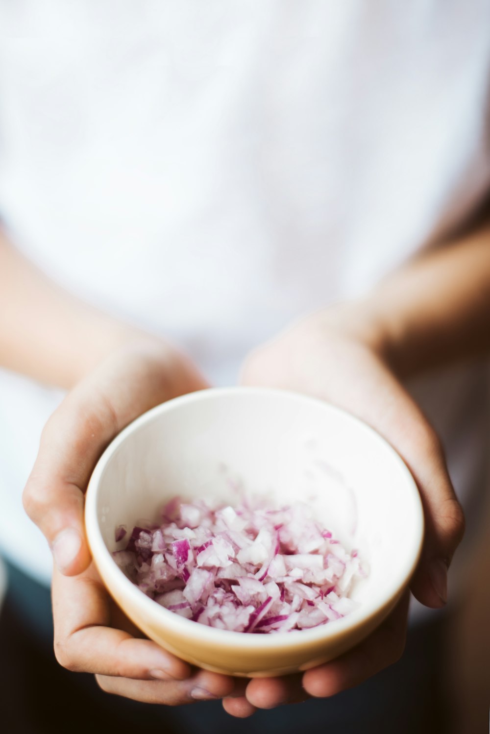 person holding ceramic bowl filled with onions