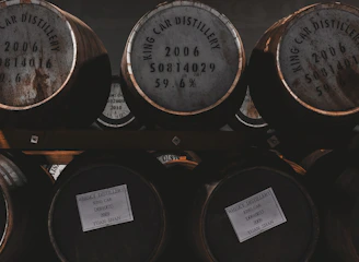 A close-up of aged whiskey barrels stacked in a dimly lit cellar, highlighting the wood grain and warm amber tones.