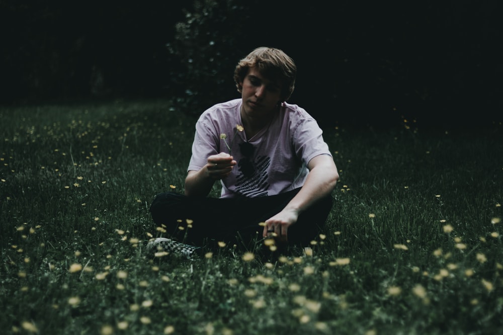 man holding flower while sitting on green grass field