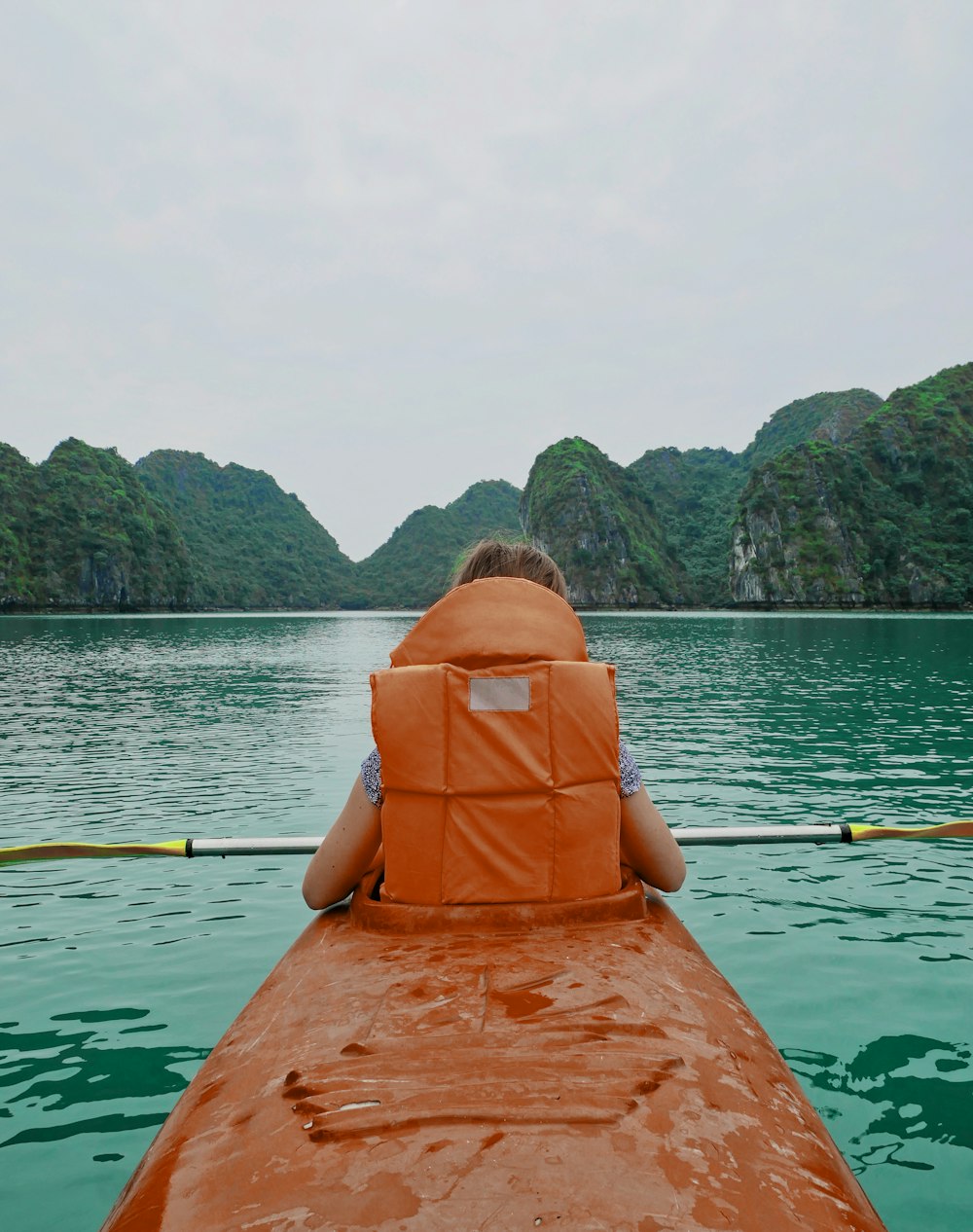 person wearing life vest riding on kayak on body of water