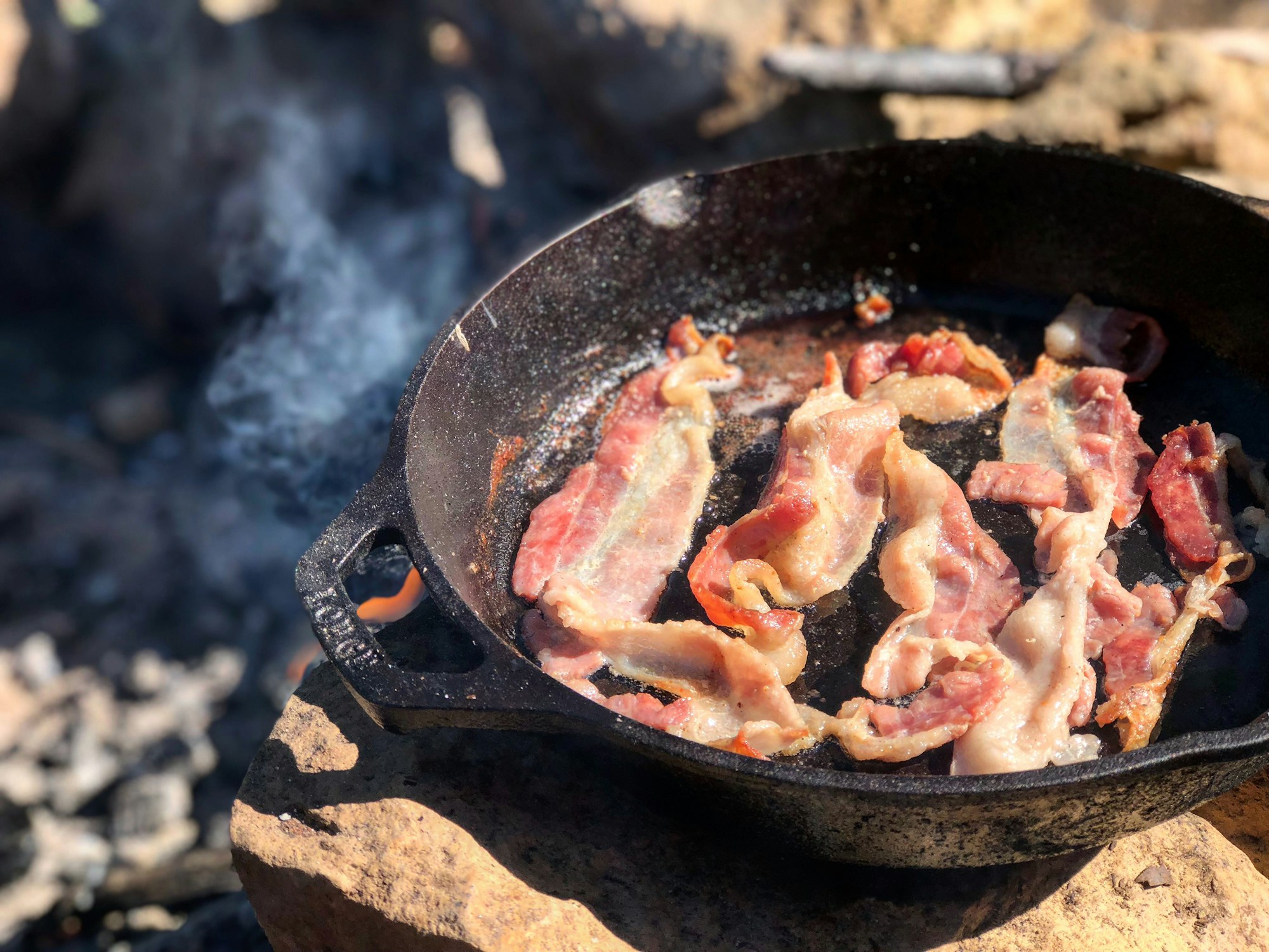 Just bought a cast iron for our summertime camping adventures.  Learning how to build a cooking efficient campfire from scratch was the ticket.  Luckily my boyfriend knows how to build the perfect one.  After an early morning of waking up and getting the fire started, a few hours later we had coals and our rocks heated to the perfect temperature. 
 This bacon took only a few minutes to cook, on the surface of a rock mind you, in just a few minutes. Mmm, bacon.