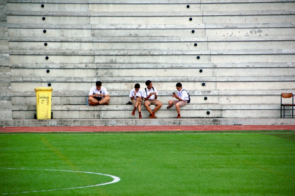 four boys wearing white shirt sitting near field