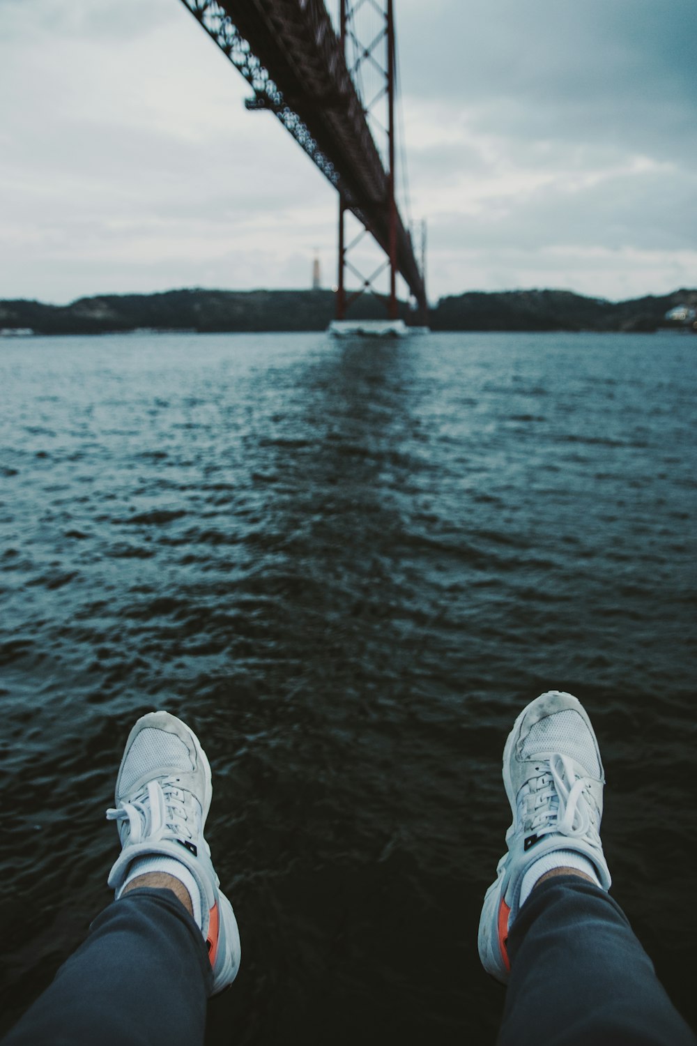 person sitting beside body of water under bridge